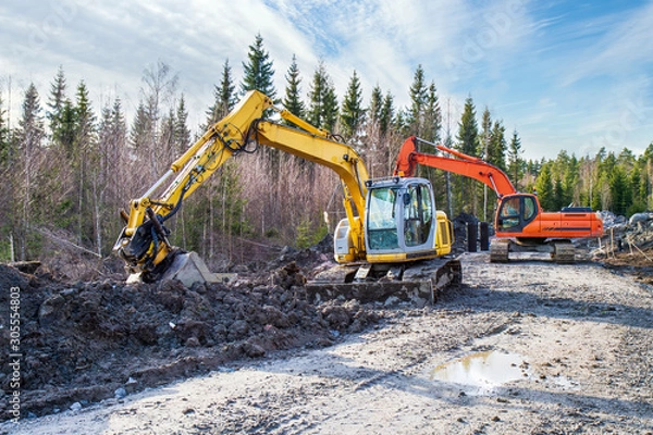 Fototapeta Yellow and orange excavator building a road deep in the forest. Rusko, Finland.