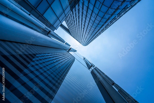 Fototapeta Bottom view of modern skyscrapers in business district against blue sky.