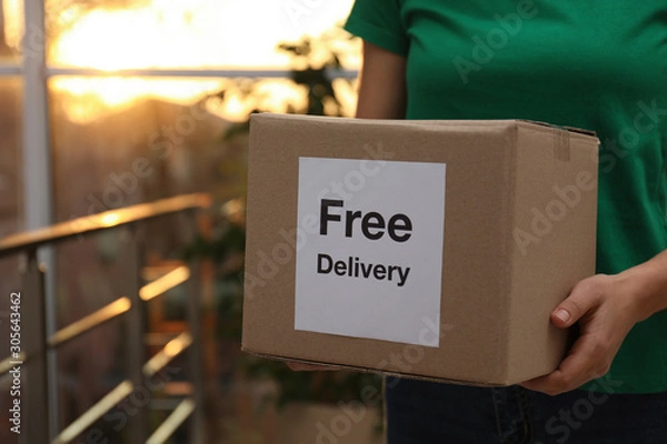 Fototapeta Courier holding parcel with sticker Free Delivery indoors, closeup