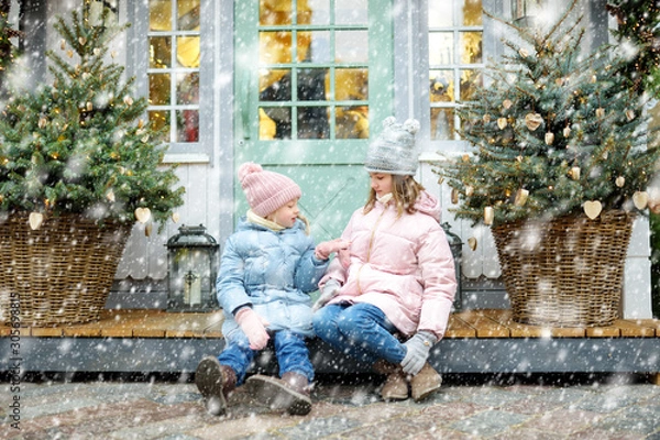 Fototapeta Two adorable sisters having a good time together on traditional Christmas fair in Riga, Latvia. Children enjoying sweets, candies and gingerbread on Xmas market.