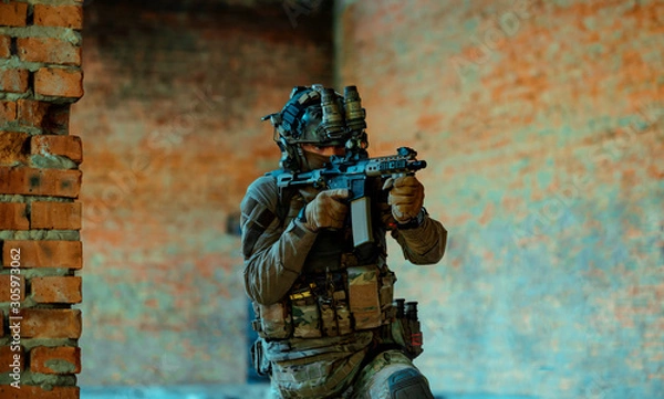 Fototapeta Man in uniform with machine gun and night-vision device, move in broken building. Airsoft soldier Aims at the sight in building. Horizontal photo