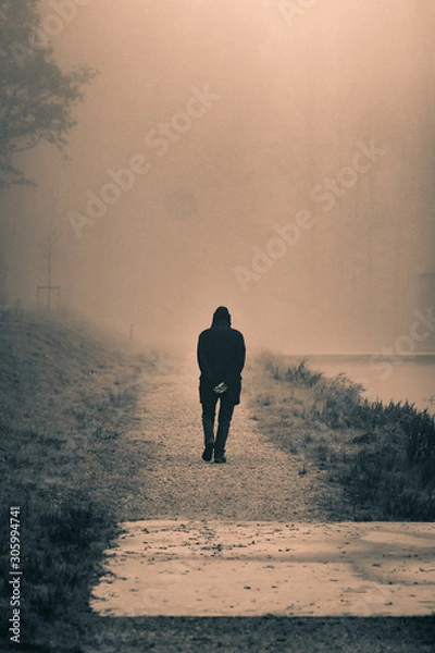 Fototapeta Old man walking down a path next to a foggy river