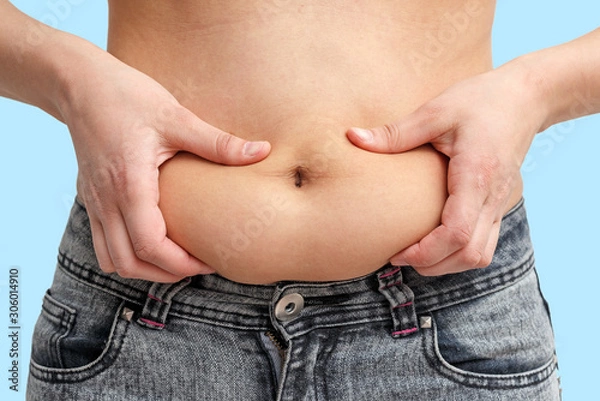 Fototapeta two hands woman holding excess fat on the stomach. on a blue background. front view