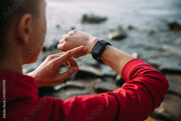 Fototapeta Concept of Biohacking, Modern Technology in Health and Sports. Woman Uses a Smartwatch on Her Hand to Train Healthy Lifestyle, View from behind