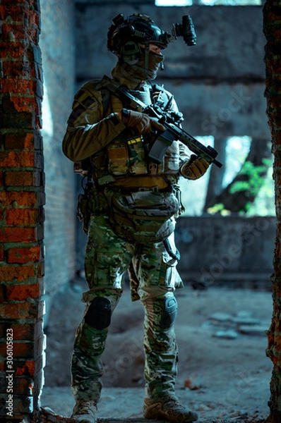 Fototapeta Man in uniform with machine gun and night-vision device inside broken building. Airsoft soldier in night building, beside two walls. Vertical photo