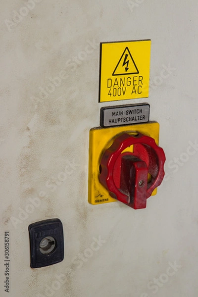 Obraz 400V  AC electricity switch bright red and yellow on industrial machine. Huge button key lock for health and safety covered in dirt and grime.