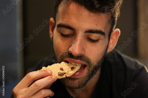 Obraz Young man with nose piercing eating chocolate cookie
