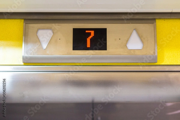 Obraz Number 7 on an elevator shaft going up or down yellow above metal electronic doors in office dirty grimy for transport using technology in factory car park