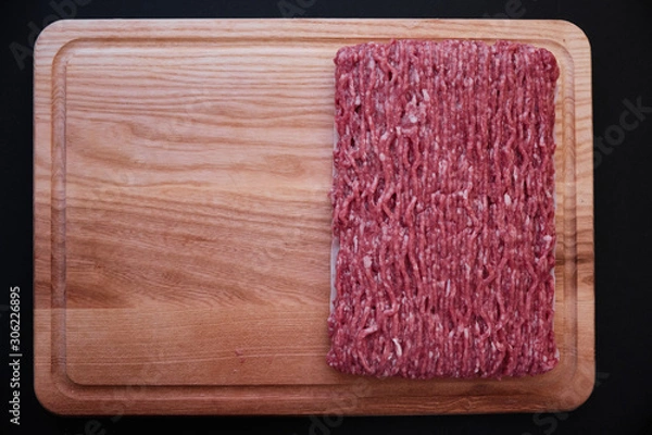 Fototapeta Raw minced pork on wooden cutting board on black background close-up. top view, copy space left
