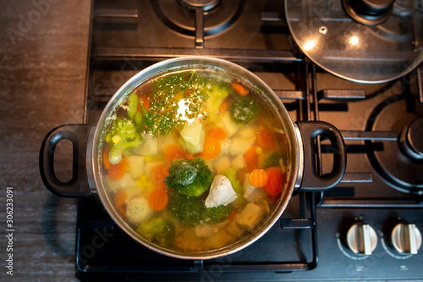 Obraz Homemade chicken vegetable soup, overhead, close-up view on a white background. bowl of fresh homemade soup to cure flu at table, top view. Vegetable soup with ingredients carrot cauliflower potato 