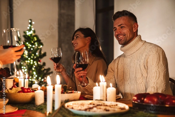 Fototapeta Photo of people drinking wine and smiling while having Christmas dinner