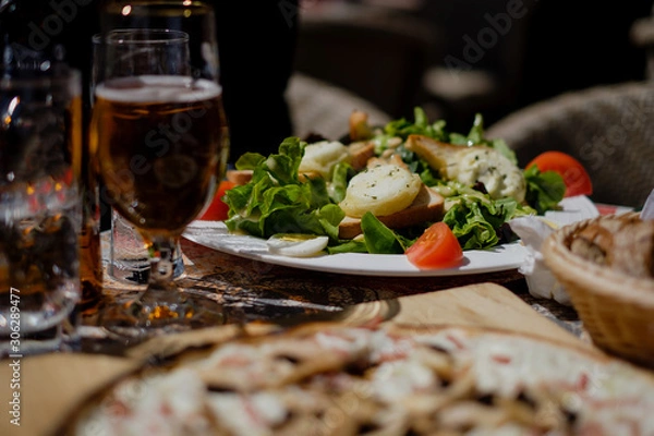 Obraz Goat cheese salad on table with beer and other delicious itens out in the sun, blurred foreground. Colmar, Alsace
