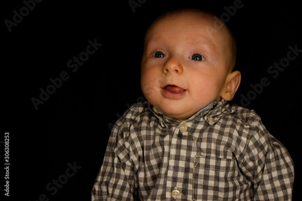Fototapeta A 4 Month Old Baby Poses on a Black Background. Perfect for Memes with Copy Space.