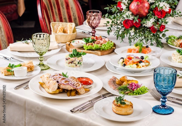 Obraz Served for holiday banquet restaurant table with dishes, snack, salads, cutlery, wine and water glasses. European food in a restaurant setting. Table set for an event party. catering