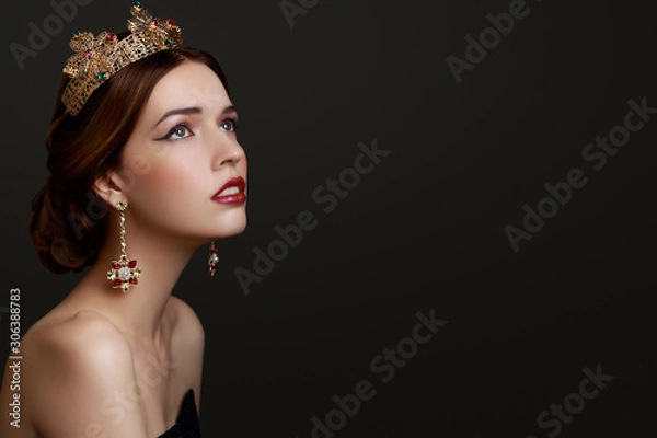 Fototapeta Beautiful girl with red lipstick in golden crown and earrings on dark background