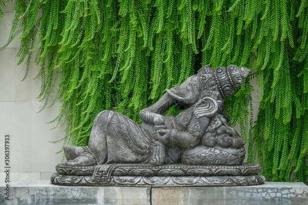 Obraz Hindu god Ganesha in lying position on a statue in front of a green and stone background.