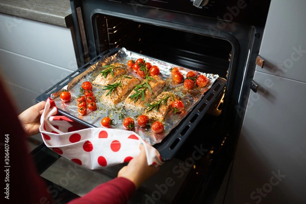 Obraz Cooking salmon in the oven. Housewife is preparing dinner. The chef is cooking red fish. Cooking fish in the oven. Girl takes out baked salmon with cherry rinds from the oven