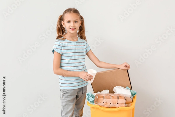 Fototapeta Little girl and container with trash on light background. Concept of recycling