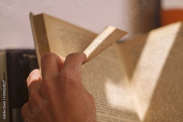 Fototapeta girl leafs through an old yellow book and bends a page with her fingers in an interesting place