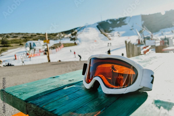 Fototapeta detail of some snowboard goggles on a green table in a ski resort full of snow and people