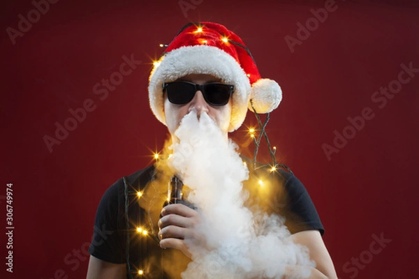 Fototapeta Vaping man in santa claus hat and a cloud of vapor