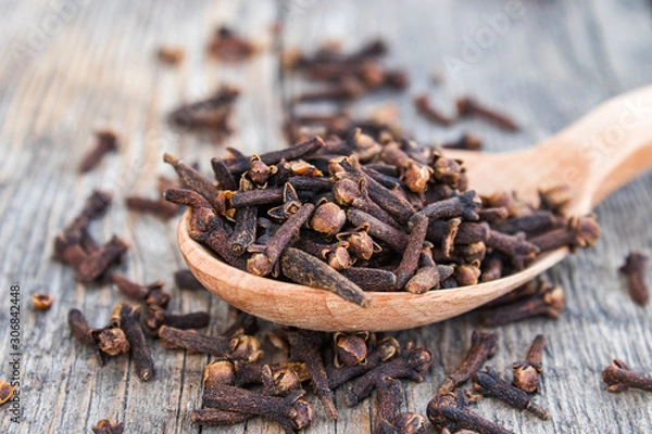 Obraz A spice of dried cloves lies on a wooden spoon and is scattered on old wooden boards.