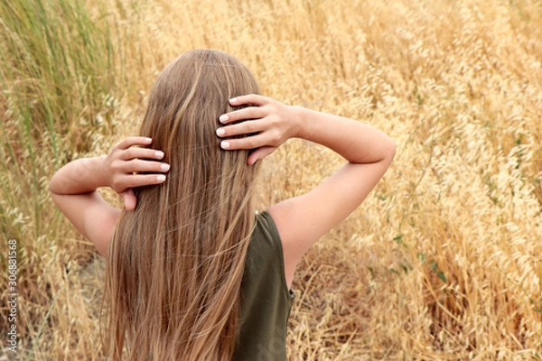 Obraz Little beautiful girl with blond hair and manicure on nails with light milk nail polish in the summer in the field.