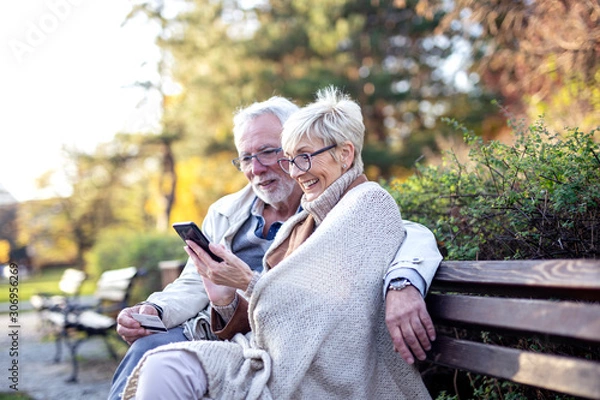 Fototapeta Senior couple shopping on line with mobile phone and credit card while sitting on the bench in park