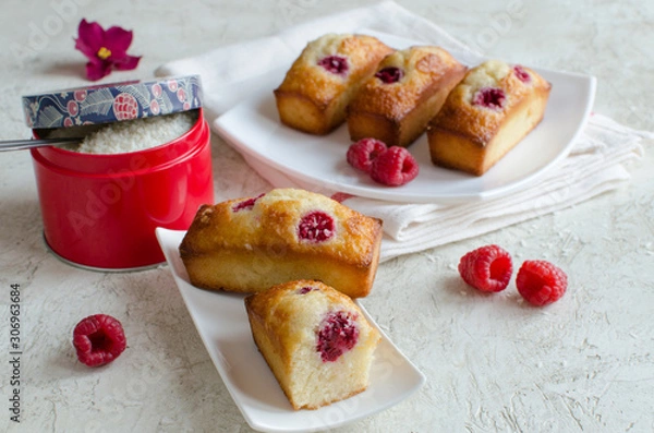 Fototapeta Financier cakes with raspberry and coconut flakes on white plate on light background