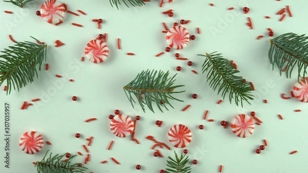 Fototapeta Christmas peppermint candy, red sprinkles and real fir or pine tree branches. Greenery with sugar sweets on white holiday table.