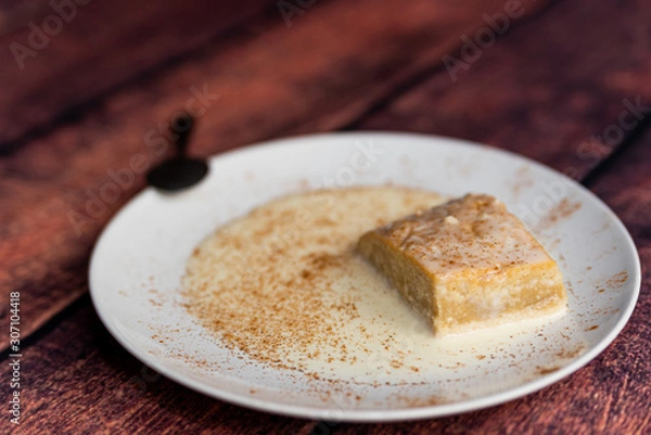 Fototapeta close up of fresh homemade "tres leches" cake, a traditional latin american dessert with milk and cinnamon powder on wooden table background with spoon