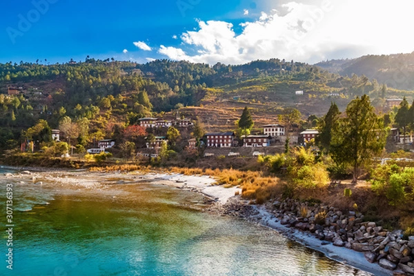 Obraz Mo Chhu River on a nice sunny day, Punakha, Bhutan. View from the wooden cantilever bridge near Punakha Dzong to river, houses of Punakha city and Himalaya mountains covered with forest.