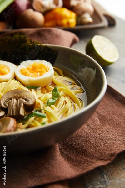 Fototapeta close up view of traditional spicy ramen in bowl on brown napkin on stone surface