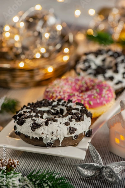 Fototapeta Pink and chocolate doughnuts lie on the Christmas table next to a candlestick. New year celebration