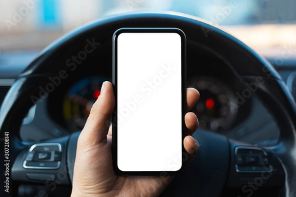 Obraz Zbliżenie: męskiej ręki trzymającej smartfon z białą makietą na ekranie, tło kierownicy samochodu.