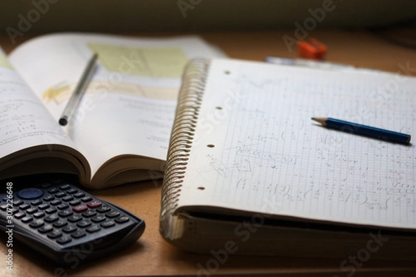 Fototapeta A notebook with math exercises written in pencil next to a calculator