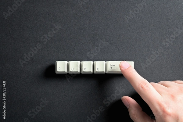 Fototapeta Computer keyboard keys with 2020 enter written using the white buttons on a dark background. Holiday technology concept. New year 2020 card.