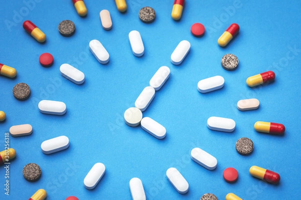 Fototapeta Group of different pills arranged in form of clock on blue background. Time in pharmacy. Time in medicine. 
