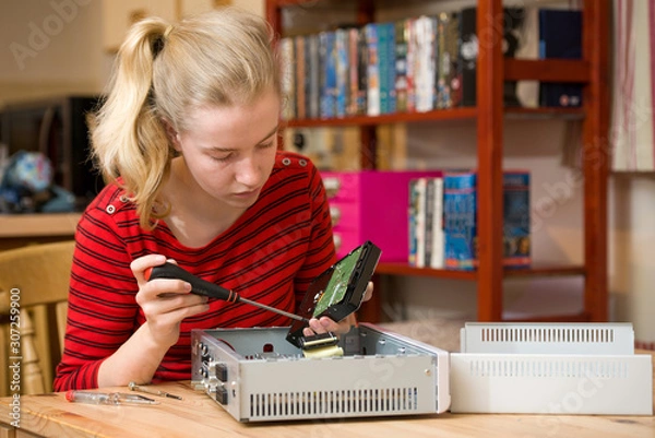 Obraz A teenage girl using a screwdriver to remove a hard drive from satellite receiver box