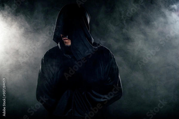 Fototapeta Man dressed in a dark robe looking like a cult leader on a smoky or foggy background.  He looks like a creepy evil villain