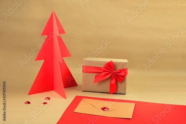 Fototapeta Gift box and envelope with red wodden Christmas tree on a natural brown background with scattered hearts.