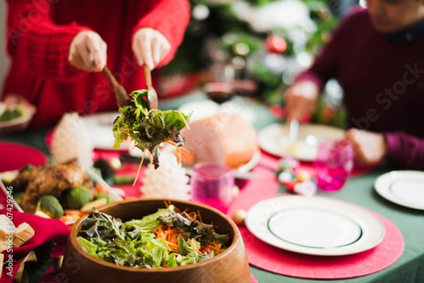 Fototapeta Young Asian family celebration in Christmas day, mother take meal salad to father which smiling and felling happy love in kitchen at home in morning time. Merry Xmas.