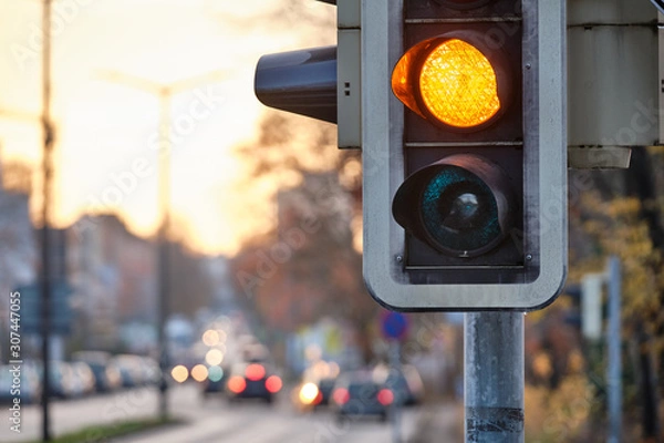 Obraz Zbliżenie sygnalizacji świetlnej o kolorze pomarańczowym do ruchu na ulicy podczas zachodu słońca. Widziane w Norymberdze, Bawarii / Niemczech w grudniu