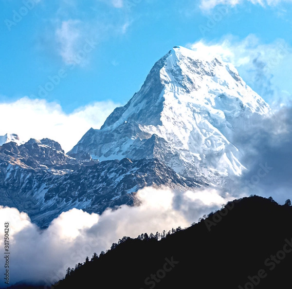 Fototapeta Amazing autumn panorama with mountains covered with snow and forest against the background of blue sky and clouds. Mount Everest, Nepal.