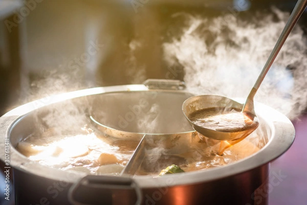 Fototapeta Cooking person in the restaurant is cooking while using the dipper in a large soup pot. And the water is boiling, there is smoke and hot spit.