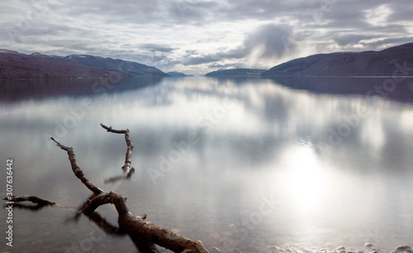 Fototapeta A view across Loch Ness looking down the length of the lake with rocks inn the foreground and dark clouds above, in Scotland, UK