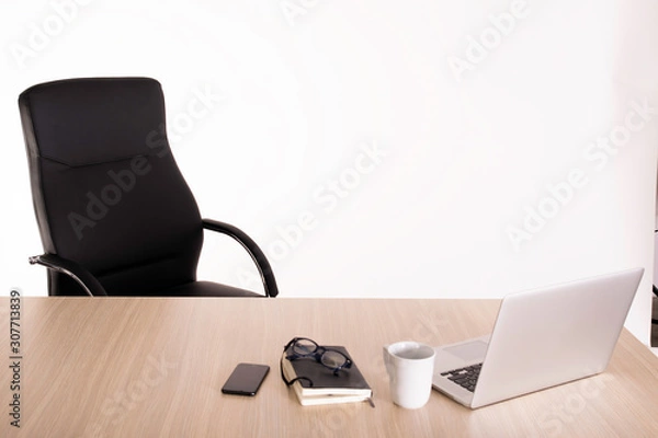 Fototapeta An empty black armchair at a wooden desk with a open laptop, cup of tea, notebook, reading glasses and mobile phone. Negative space. Copy space area for advertising.
