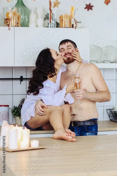 Obraz couple in the kitchen with christmas decoration, drink champagne, celebrate new year