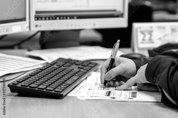 Obraz London, England, 28/01/2019 Black and White young woman working in an office doing administrative paperwork. close up of her hands writing with a pen on paper coloured fingernails and keyboard on desk