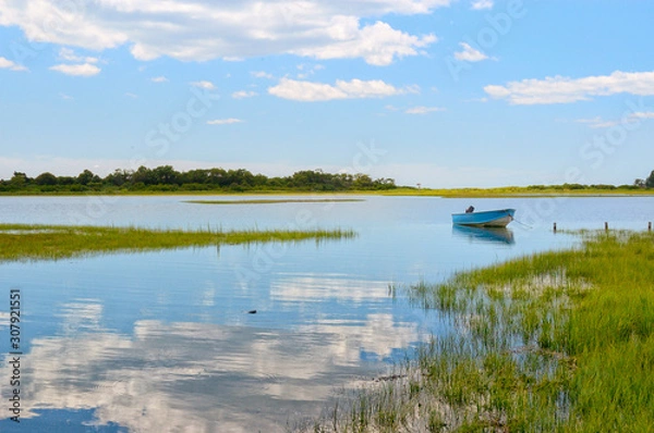 Fototapeta Tranquil view Niantic Connecticut salt marsh in summer with blue sky and blue boat reflections of cumulus clouds in still water with copy space, saltwater tidal marsh, East Lyme, New England scenic